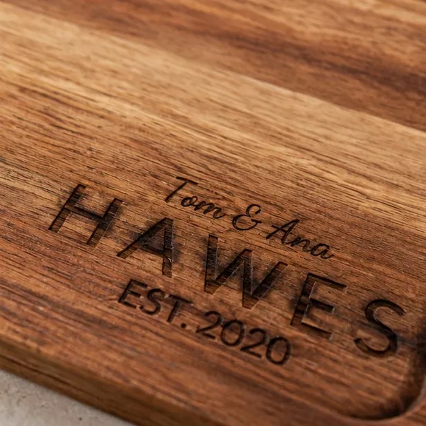 An engraved acacia cutting board on a kitchen counter with the family name burned into it