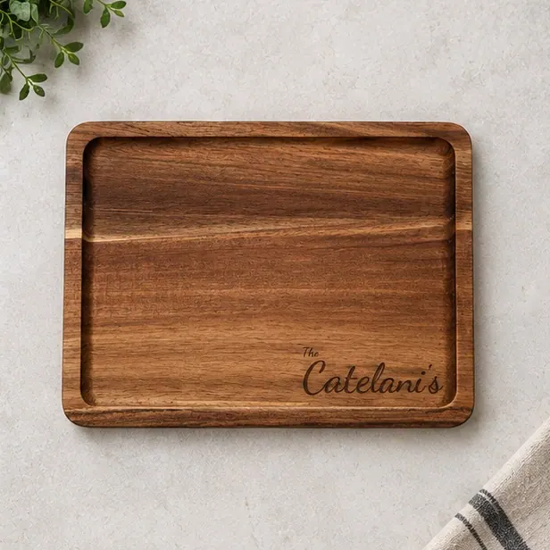 An acacia board engraved with a script family name, photographed from above on a pale stone counter